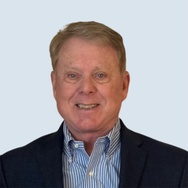 Jim is a light-skinned man with short blonde hair and blue eyes. He is wearing a black suit jacket over a striped blue and white collared shirt. He is pictured smiling against a grey-blue background.