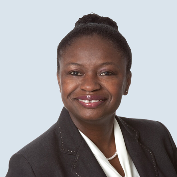 Livia is a dark-skinned African-American woman with short curly hair pulled up into a bun. She is smiling and looking straight into the camera. She is dressed in a dark blue business suit with a white, collarless blouse, a string of pearls and pearl earrings. She is pictured against a blue-grey background.