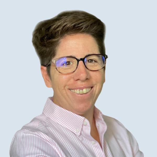 Graciana is a light skinned woman. She has short brown hair, glasses and wears a pink-striped collared shirt. She is smiling in front of a blue-grey background.