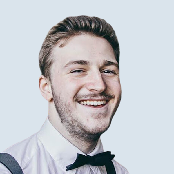 Kevin is a light-skinned man with short brown hair. He is smiling wide in a white dress shirt and tie. He is pictured against a blue-grey background.